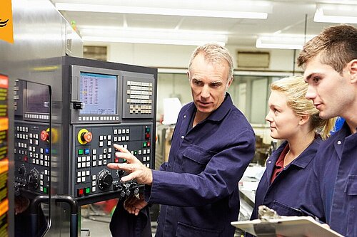 A man in the centre of the image shows a woman and a man on the right of the image a machine