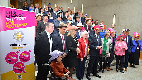 MSPs stand in rows in the Scottish Parliament wearing hats